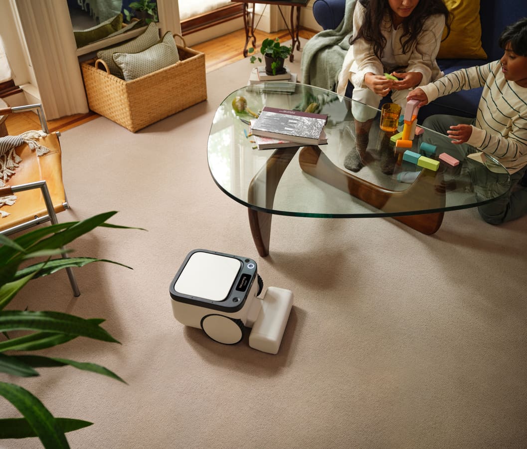 A family in a living room, children playing with wooden blocks at a glass coffee table while the Matic cleans the carpet nearby
